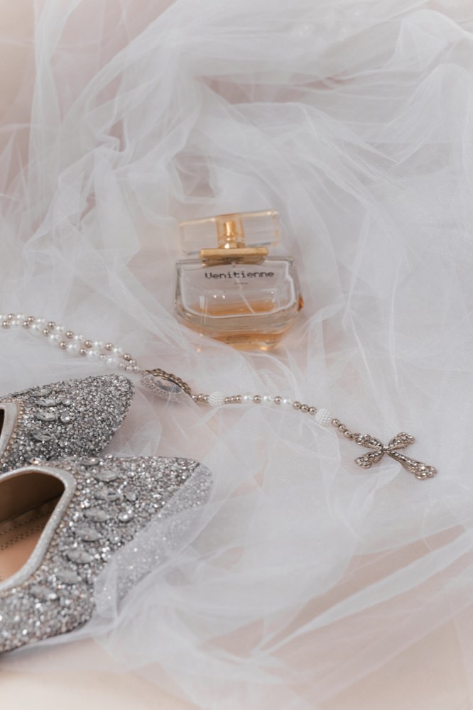 Perfume, terço e sapato da noiva sobre o véu
